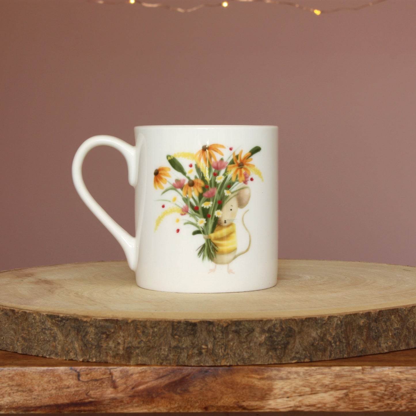 A white bone china mug showing an illustration of a mouse in a yellow striped jumper holding a colourful bunch of flowers. 